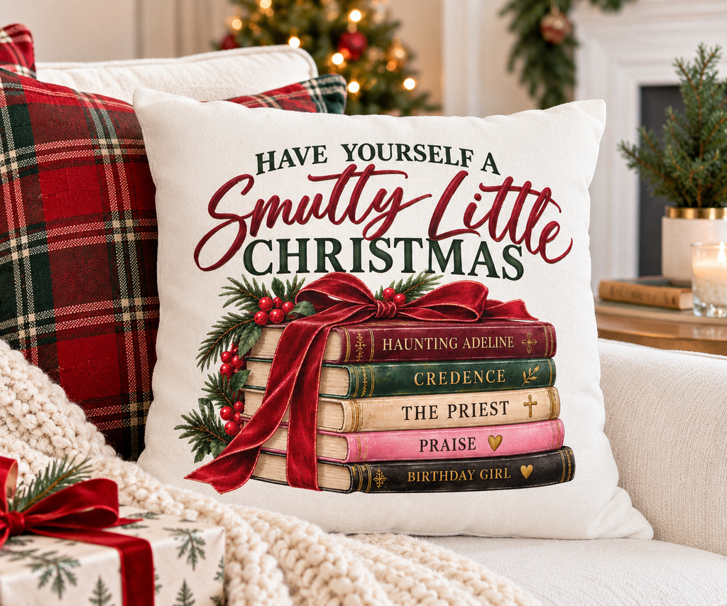 Have Yourself a Smutty Little Christmas book lover pillow styled on a green reading chair beside books and a holiday mug with a Christmas tree and fireplace behind it.