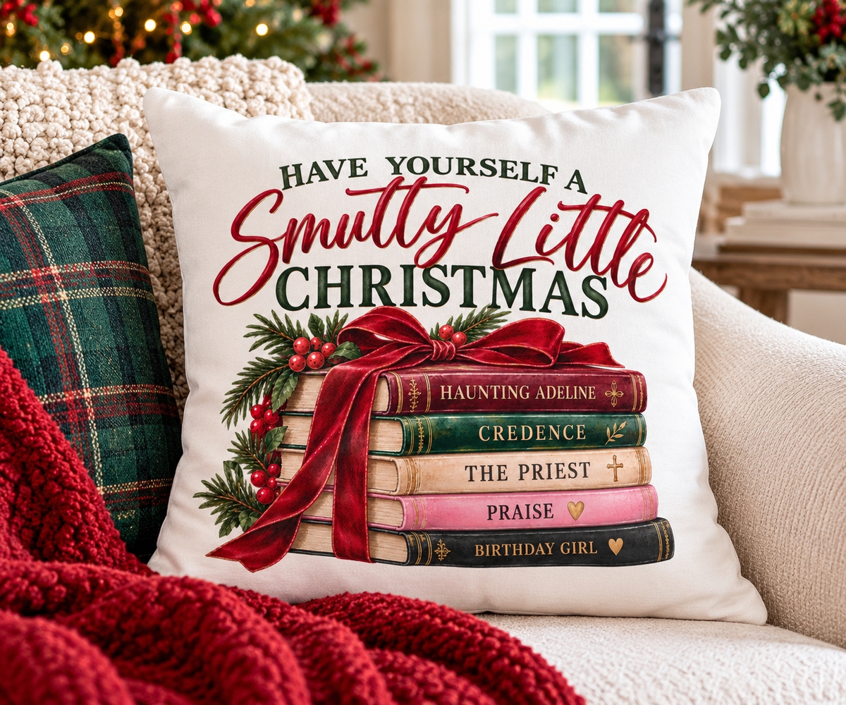 Have Yourself a Smutty Little Christmas book lover pillow styled on a green reading chair beside books and a holiday mug with a Christmas tree and fireplace behind it.