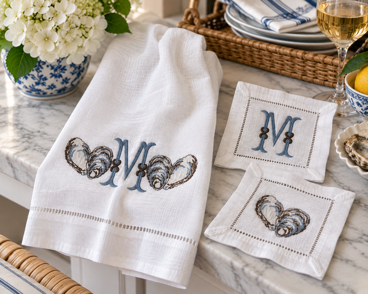 Coastal embroidered linen towel and cocktail napkins with oyster shell motifs, dusty blue monogram, hemstitched edges and natural linen texture.