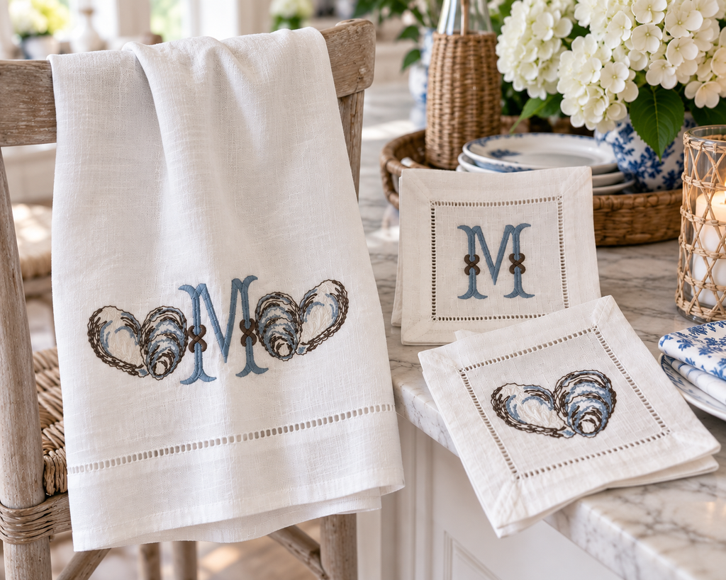 Coastal embroidered linen towel and cocktail napkins with oyster shell motifs, dusty blue monogram, hemstitched edges and natural linen texture.