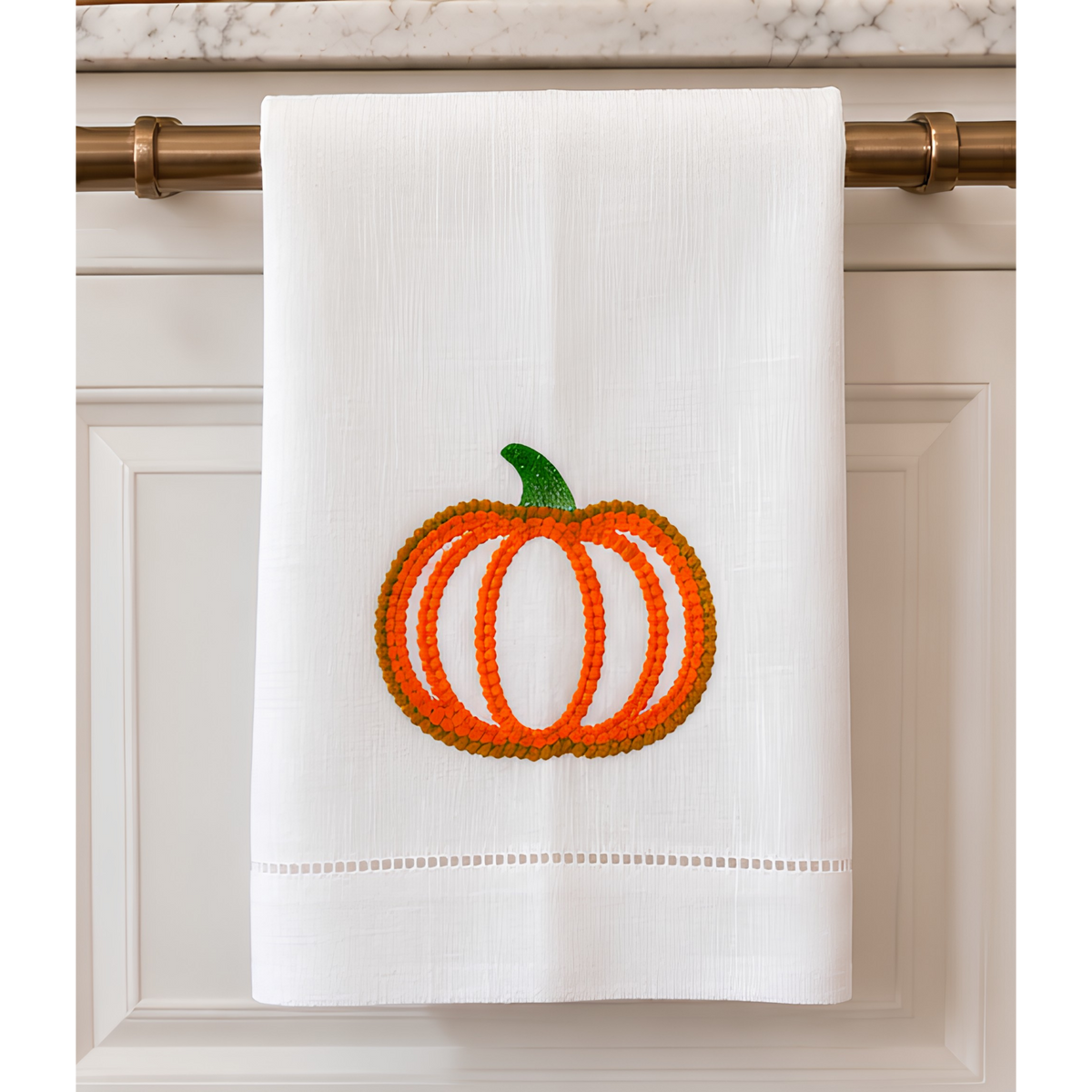 White 14 by 22 linen kitchen towel with textured orange and golden embroidered pumpkin, green stem and decorative hemstitch border.