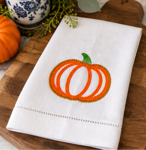 Embroidered pumpkin linen kitchen towel styled in a bright fall kitchen with white cabinetry and seasonal autumn accents.