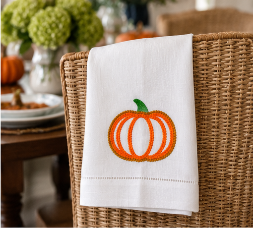 White hemstitched linen kitchen towel featuring orange pumpkin embroidery styled as elegant Thanksgiving kitchen decor.